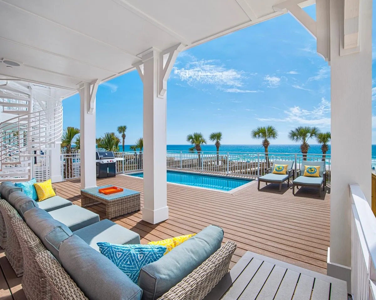 A private, heated pool sits just steps from the villa, surrounded by a comfortable outdoor seating area and shaded by palm trees. A spiral staircase and built-in barbecue grill are visible, with the sparkling ocean just beyond. The space is set up for alfresco lounging and memorable poolside gatherings.